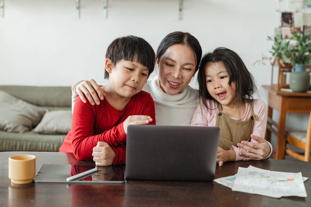 adorable little ethnic children watching funny video on laptop with mother