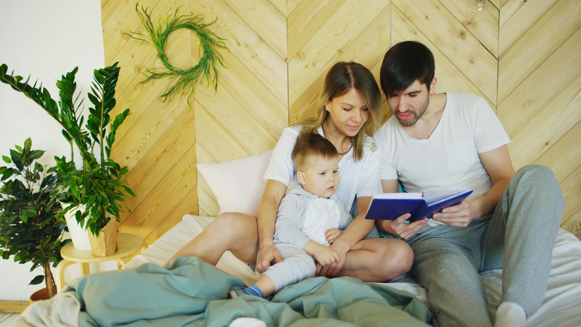 parents and their little son reading a book in bed